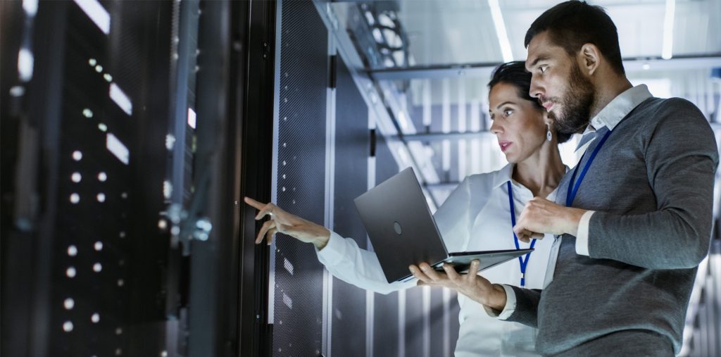 Man and woman IT expert looking at server with laptop in hand